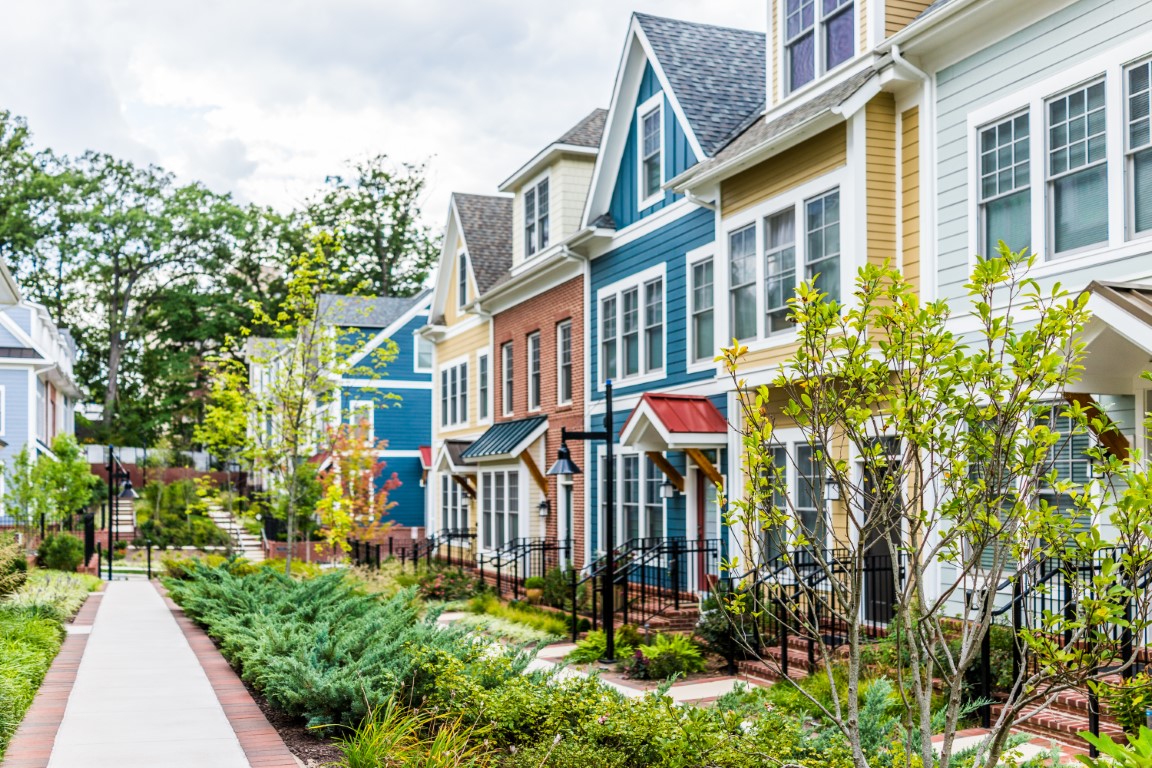 A beautiful row of houses on either side of a sidewalk, with a garden in front of each.